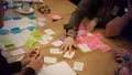 Overhead view of hands sorting colored sticky notes and cards on a table during a planning workshop.