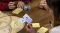 Close-up of a hand holding the blue "Organisation" EDGY game card above the wooden game board, with sticky notes and a drink nearby.