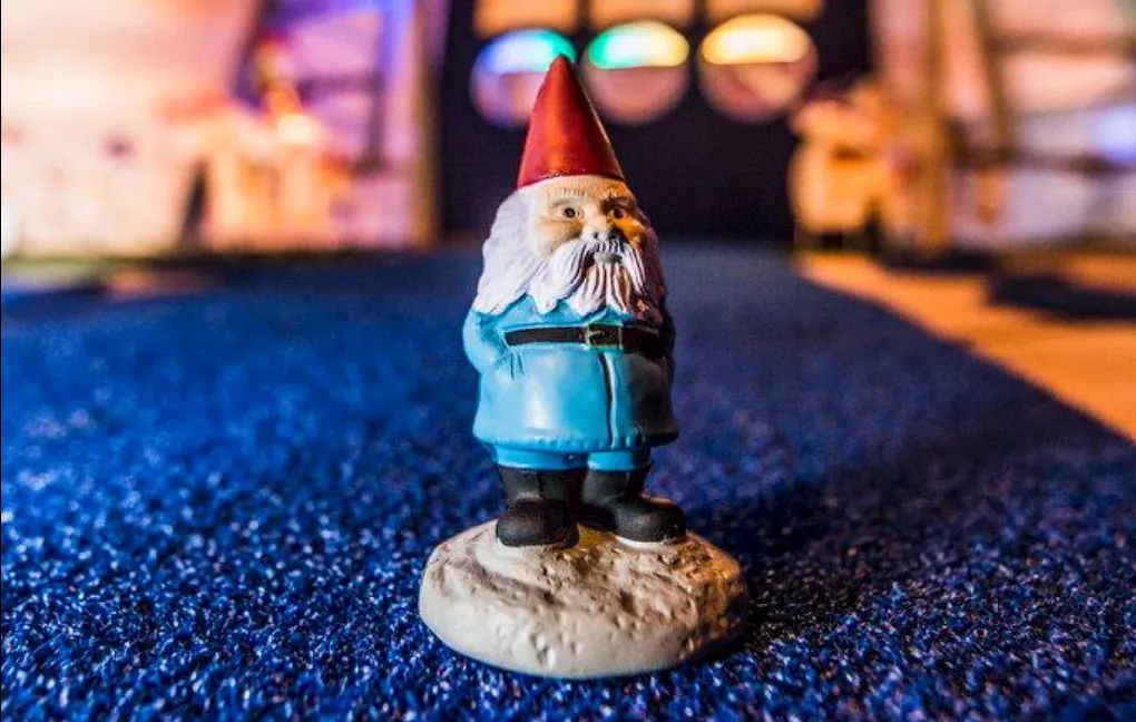 A small garden gnome figurine standing on blue carpet, lit by colorful blurred lights.