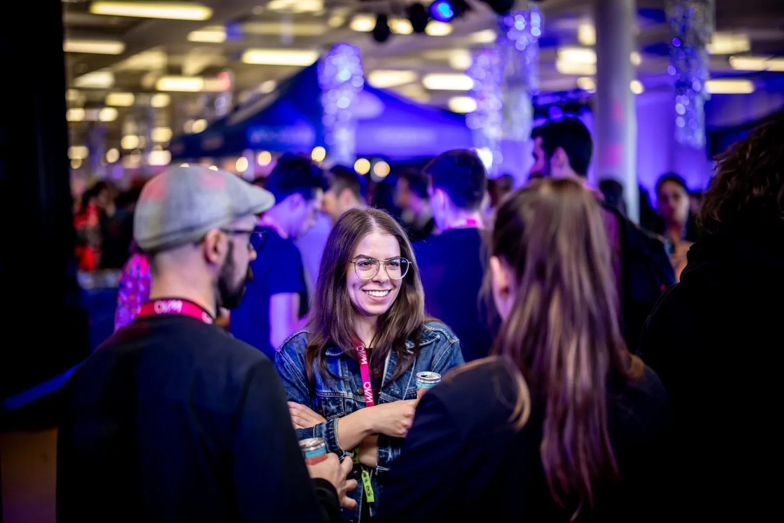 A woman smiling in conversation with others at a night event under purple lighting.