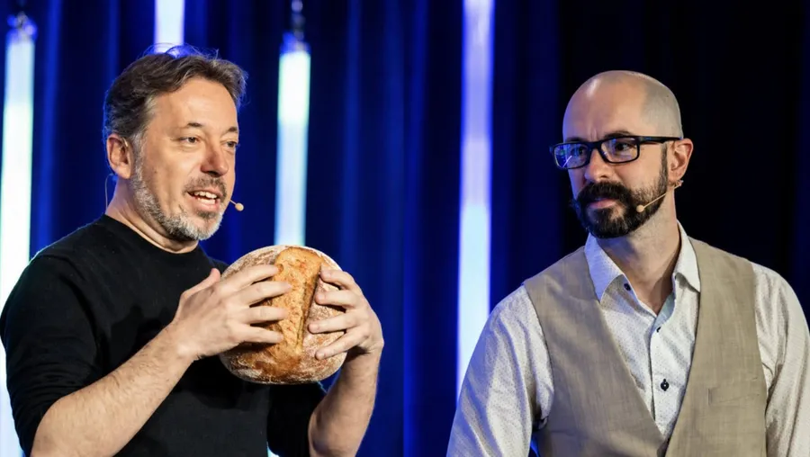 Éric Letarte holding up a loaf of bread on stage, JS Daigle beside him